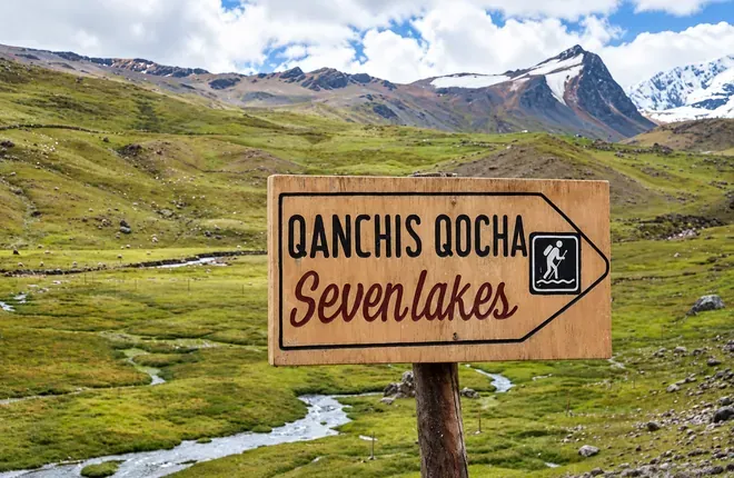 Wooden sign reading Qanchis Qocha, Seven Lakes, in a green valley
