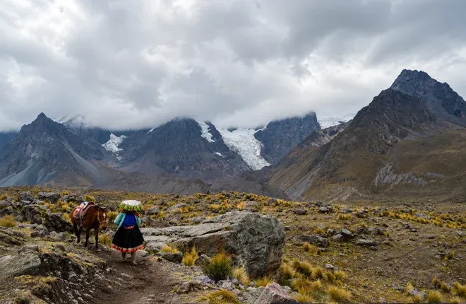 Local woman leading a horse along the trail under cloudy peaks