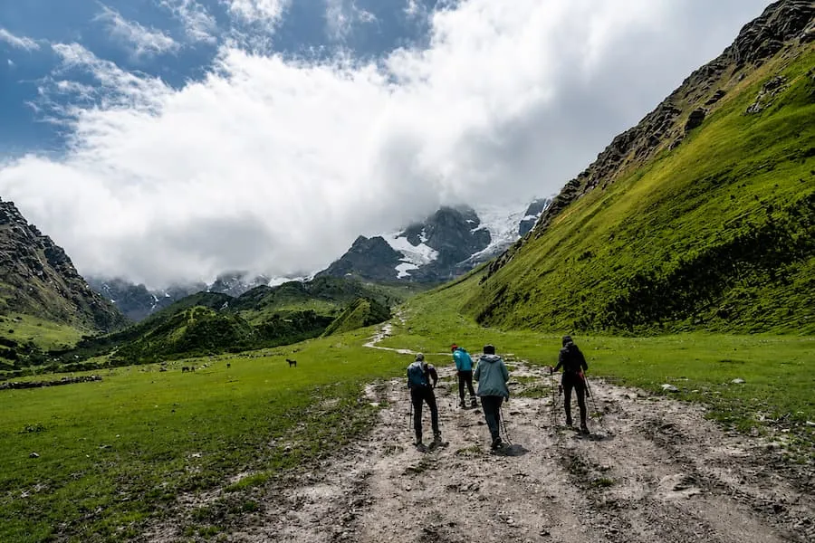 Hikers crossing a green valley toward Humantay Lake with horses grazing nearby
