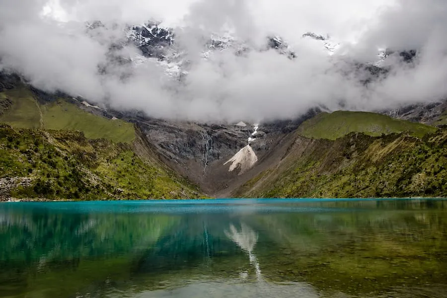 Still water of Humantay Lake reflecting ice and cloud