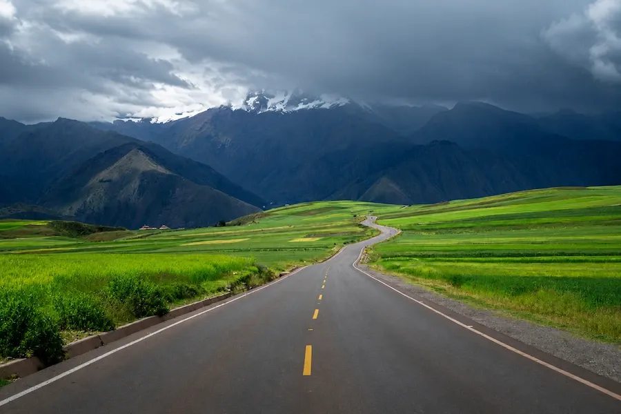 Road through green farmland in the Sacred Valley with mountains ahead