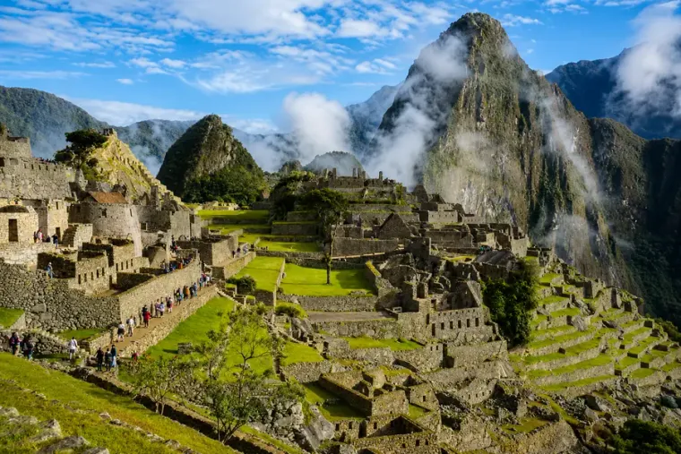 Machu Picchu in sunshine with visitors on the terraces and Huayna Picchu in cloud