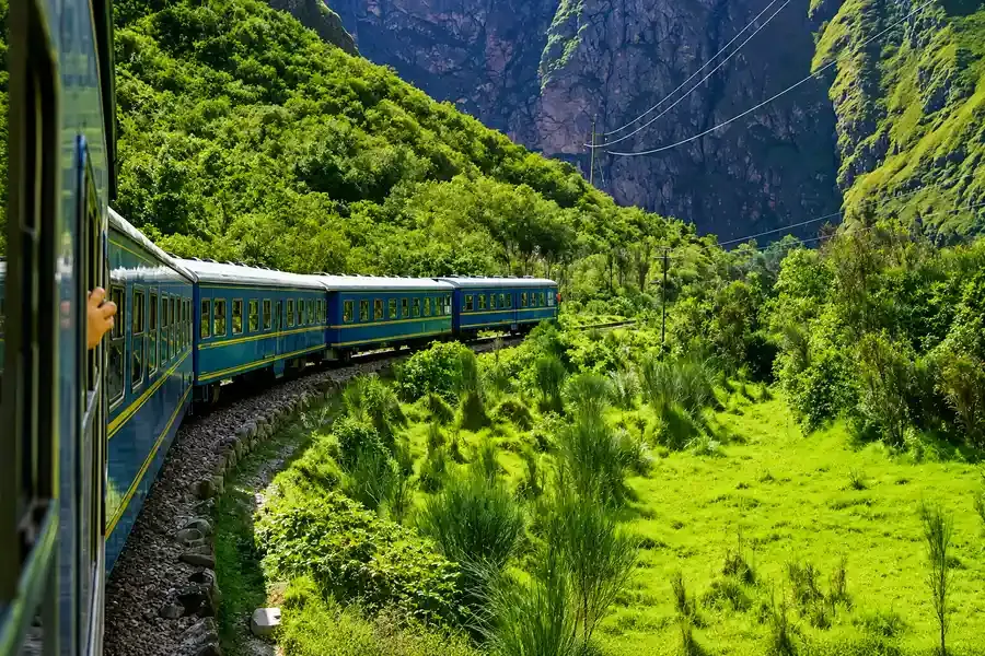 Blue train carriages curving through a green canyon, seen from a window