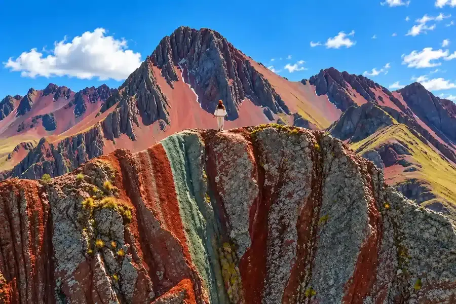 Hiker standing on bands of red, grey and green rock at Pallay Punchu