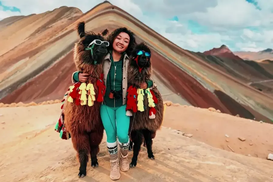 Smiling hiker next to two llamas wearing sunglasses at Rainbow Mountain