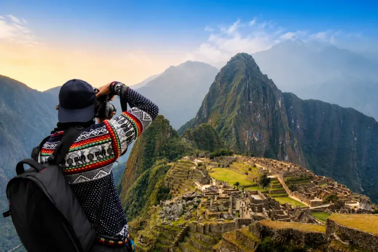 Traveler photographing Machu Picchu and Huayna Picchu in warm evening light