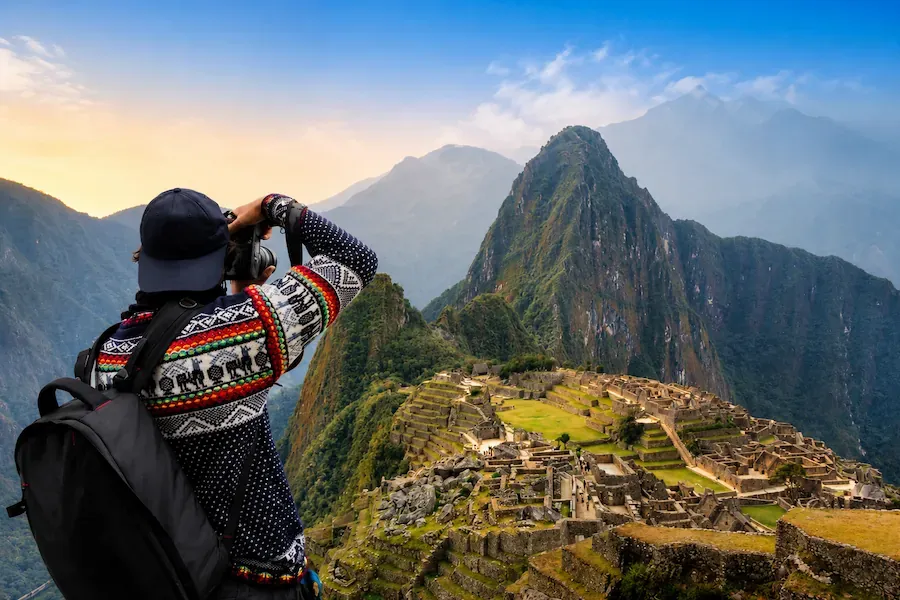 Traveler photographing Machu Picchu and Huayna Picchu in warm evening light