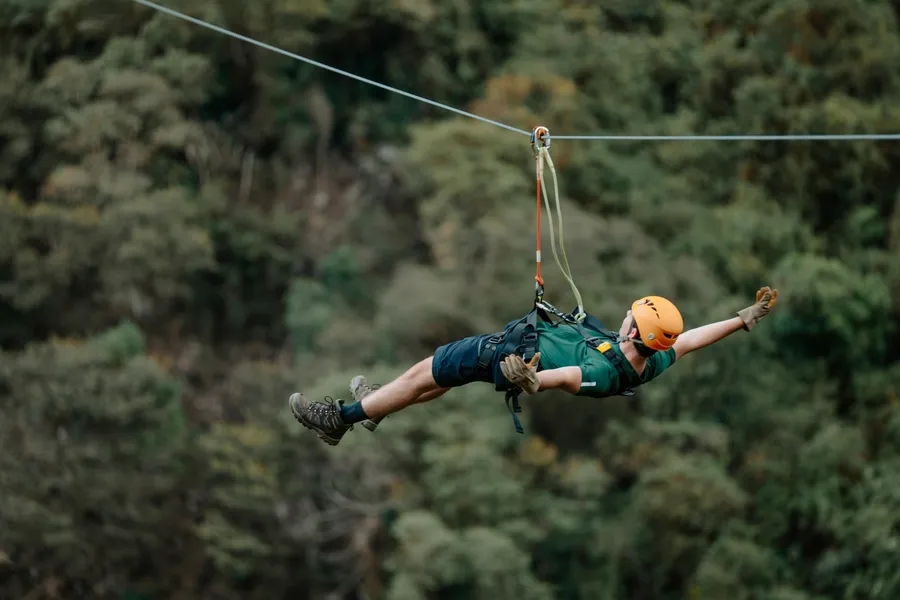 Hiker in a helmet flying face down along a zipline over the forest