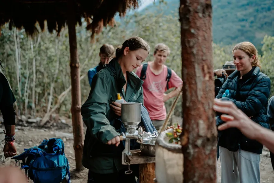 Hiker grinding coffee with a hand mill while the group looks on