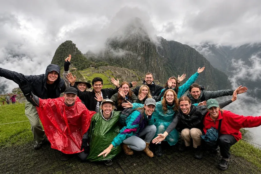 Group in rain ponchos cheering in front of a cloudy Machu Picchu