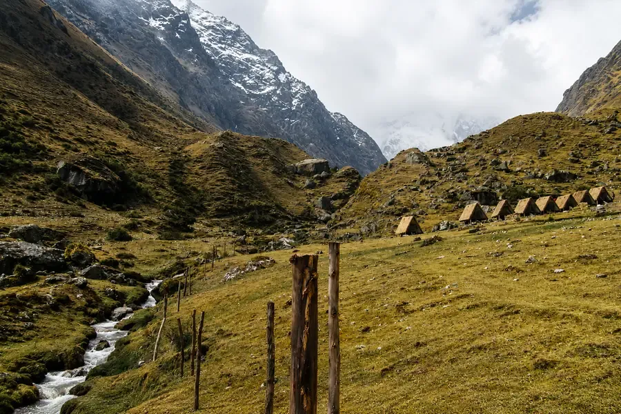 Row of thatched huts in a green valley beside a mountain stream